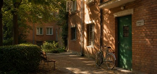 Early morning light in the inner courtyard of a mid-century student residence hall in a Romanian university city. A single bicycle leans against a warm brick wall next to a green painted metal door. Tall lime trees cast soft dappled shadows over concrete paving, with a low clipped hedge and an empty wooden bench nearby. Quiet late summer atmosphere, a few fallen leaves, open windows on the upper floors. Eye level view, shallow depth of field, warm golden sunlight raking across the brickwork. Use balanced, natural contrast with a realistic tonal range. Preserve fine detail throughout the image, with smooth highlight roll-off, detailed shadows, balanced exposure, and natural, accurate colors.